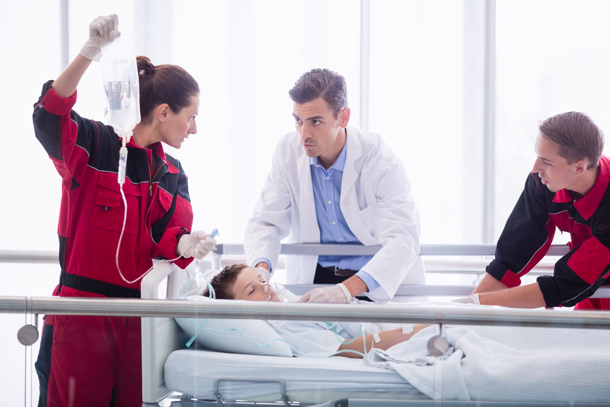 Medical personnel, including top medical students on their Emergency Medicine rotations, administering emergency care in a hospital setting to a young female patient in a bed, with one holding an IV bag.