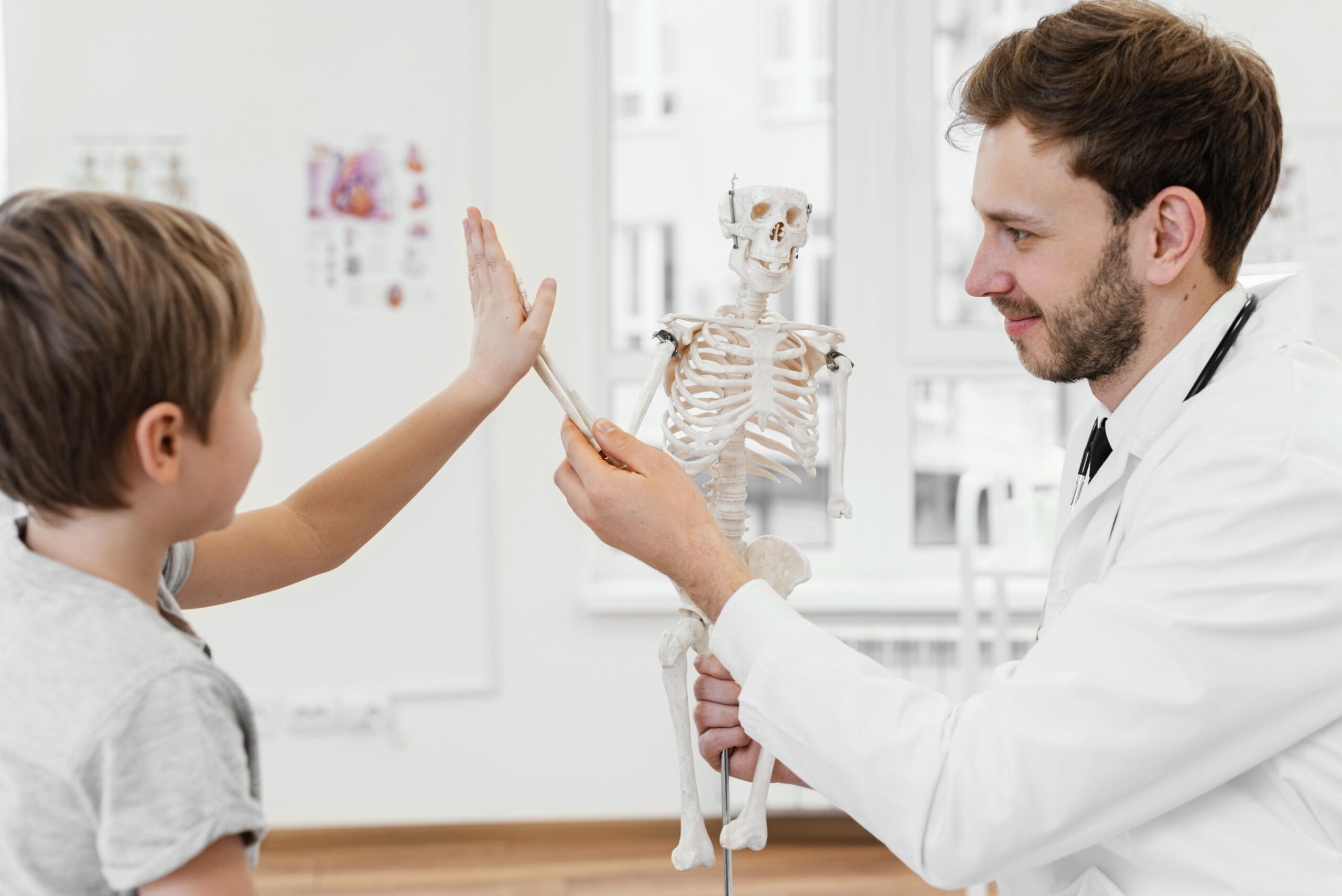 A smiling medical professional in a white coat holds a small skeleton model, receiving a high-five from a child, embodying ideals from the Pediatrics Rotation Guide in a clinical setting.