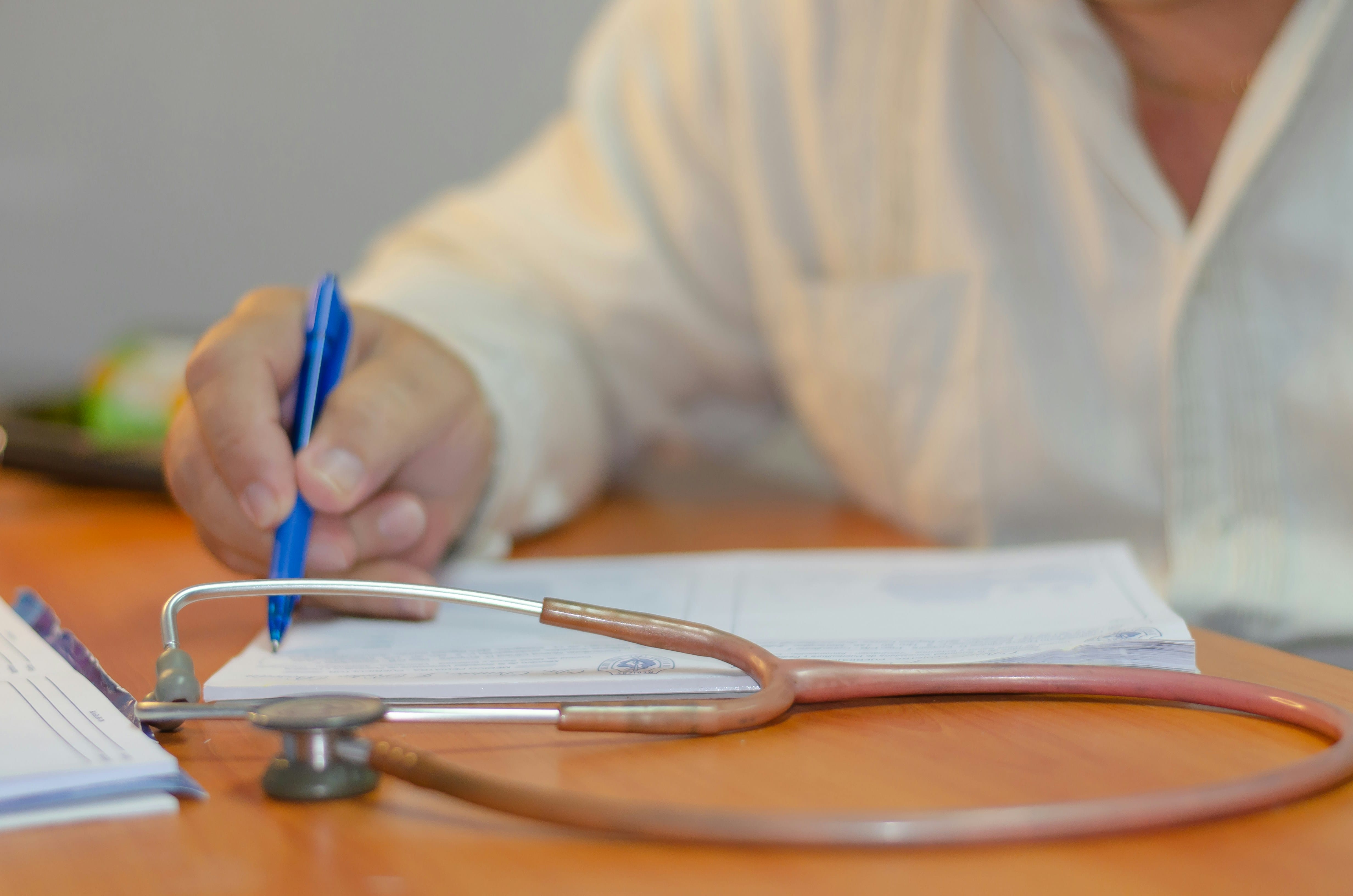 A person in a white shirt writes on paper at a desk with a stethoscope lying in the foreground, reflecting on clinical teaching and the role of preceptors in combating physician burnout.
